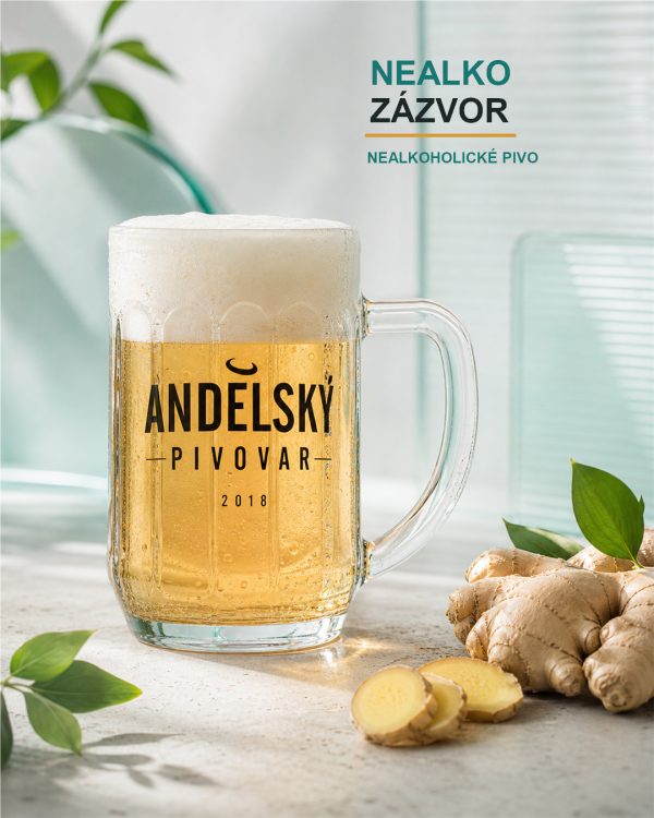 Fazetovaný půllitr Andělského pivovaru s nealkoholickým zlatavým pivem stojí vedle čerstvého zázvoru a nakrájených zázvorových plátků.