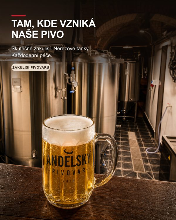 Fazetovaný půllitr světlého piva s logem Andělského pivovaru stojí na dřevěném pultu před nerezovými tanky ve skutečném sklepním provozu pivovaru.