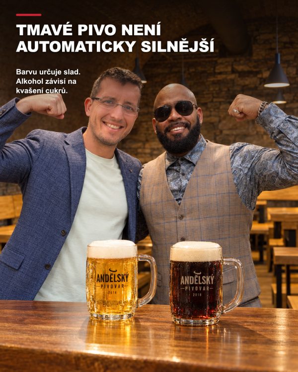 Dva usměvaví přátelé v klenutém sklepě Andělského pivovaru žertem ukazují svaly za stolem, na kterém stojí půllitr světlého a půllitr tmavého piva.